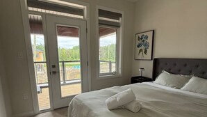 A bedroom with a bed, a nightstand, a painting, and a door leading to an outdoor area. - Modern Orillia Retreat - W/ Game Room (Severn)
