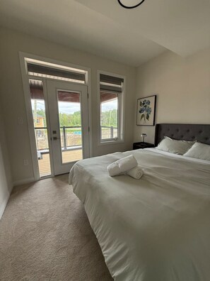 Quarto com cama, mesa de cabeceira, um quadro e porta que dá para uma área externa.