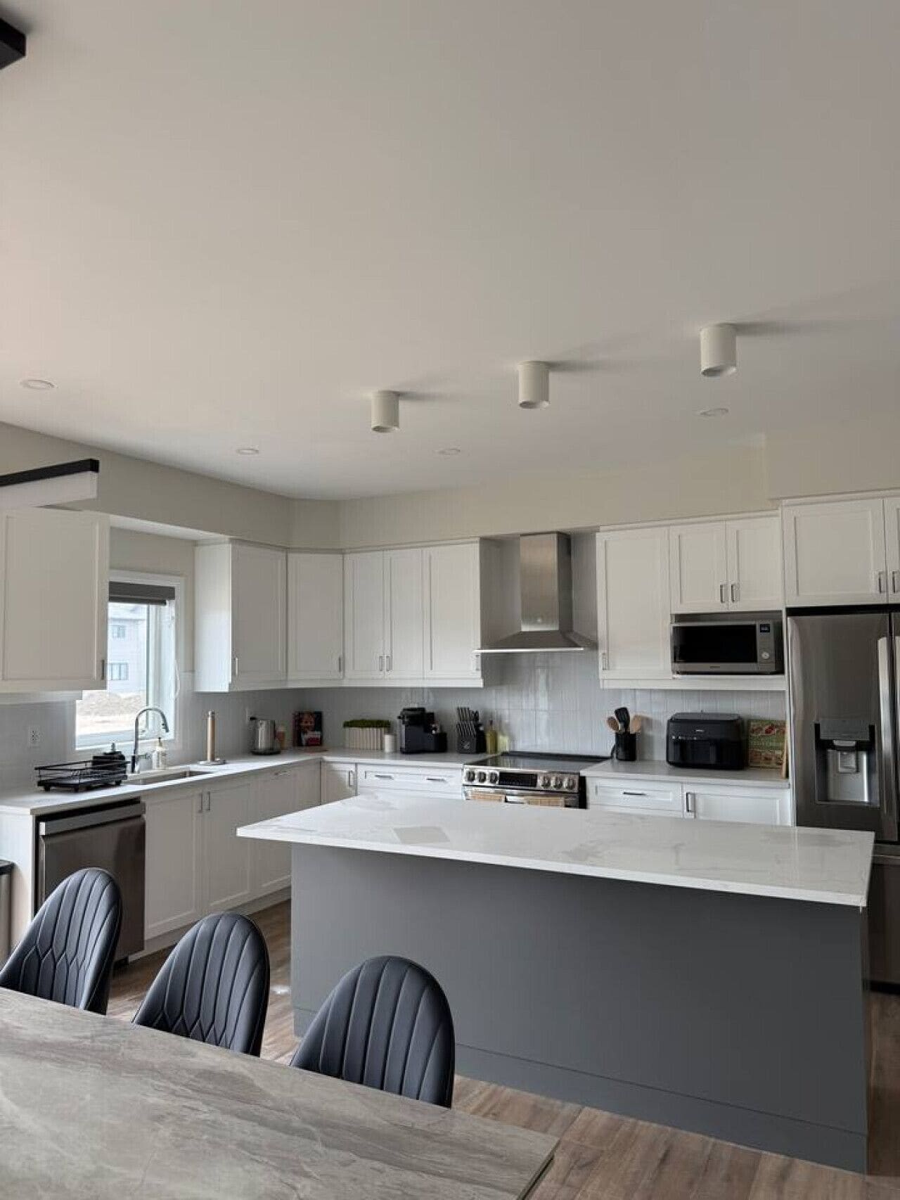 Una cocina moderna con armarios blancos, una isla central, electrodomésticos de acero inoxidable y un comedor con sillas.