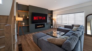 A modern living room with a large flat-screen TV, a fireplace, a sofa, and a coffee table. - Modern Orillia Retreat - W/ Game Room (Severn)