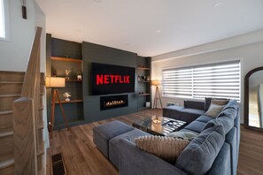 Uma sala de estar moderna com uma televisão de tela plana grande, lareira, sofá e mesa de centro.