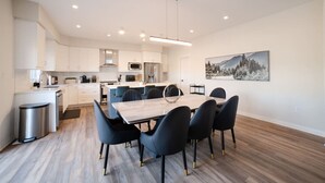 A modern kitchen with white cabinets, a central island, and a dining area with a wooden table and black chairs. - Modern Orillia Retreat - W/ Game Room (Severn)