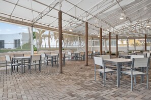 An outdoor patio area with tables and chairs, a brick floor, and a view of palm trees and buildings. - Luxury Beachfront Escape, Sunny Isles (Sunny Isles Beach)