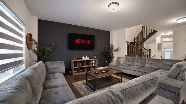 Ein modernes Wohnzimmer mit einem grauen Ecksofa, einem Couchtisch, einem Bücherregal und einer Treppe.