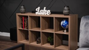 Ein Bücherregal aus Holz mit dem Wort 'Lake' obenauf, gefüllt mit Büchern, einem Globus und dekorativen Gegenständen.