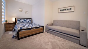 Ein Schlafzimmer mit einem Bett, einem Nachttisch, einer Lampe, einem Sofa und einem Wandbild.
