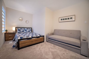 Um quarto com cama, mesa de cabeceira, luminária, sofá e um quadro na parede.