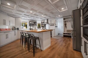 Una cocina con armarios blancos, una isla de madera con taburetes altos, un refrigerador de acero inoxidable y un horno empotrado.