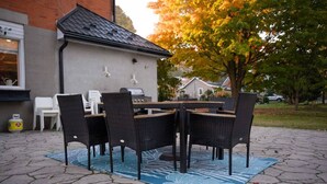 Eine Terrass mit Tisch und Stühlen, einem Grill und einem Haus im Hintergrund.