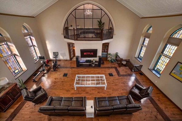A spacious living room with a large TV, leather sofas, a coffee table, and a balcony with a railing.
