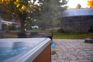 A hot tub in a courtyard with stone paving, a wooden fence, and a building in the background.