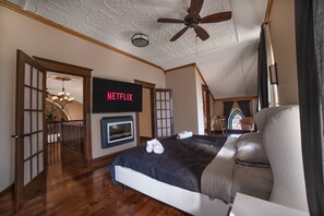 A bedroom with a bed, a television mounted on the wall, a ceiling fan, and a view of a balcony.