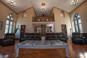 A spacious living room with leather sofas, a glass coffee table, and a high ceiling with chandeliers.