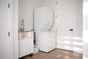 A compact laundry room with a washing machine, a sink, and a laundry basket. - Percy Boom Luxury Home:  Hot Tub/ Sauna/ Game Room (Campbellford)