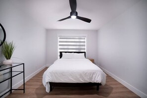 A bedroom with a bed, a ceiling fan, a window with blinds, a bedside table, and a potted plant. - Percy Boom Luxury Home:  Hot Tub/ Sauna/ Game Room (Campbellford)