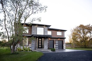 A modern two-story house with a stone facade, large windows, and a garage. - Percy Boom Luxury Home:  Hot Tub/ Sauna/ Game Room (Campbellford)