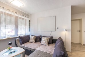 Ett modernt vardagsrum med en soffa, ett litet bord med en vas och ett fönster med persienner.