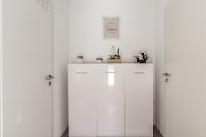 En hall med en vit dörr, ett inramat, inspirerande citat på väggen och ett litet bord med dekorativa föremål.