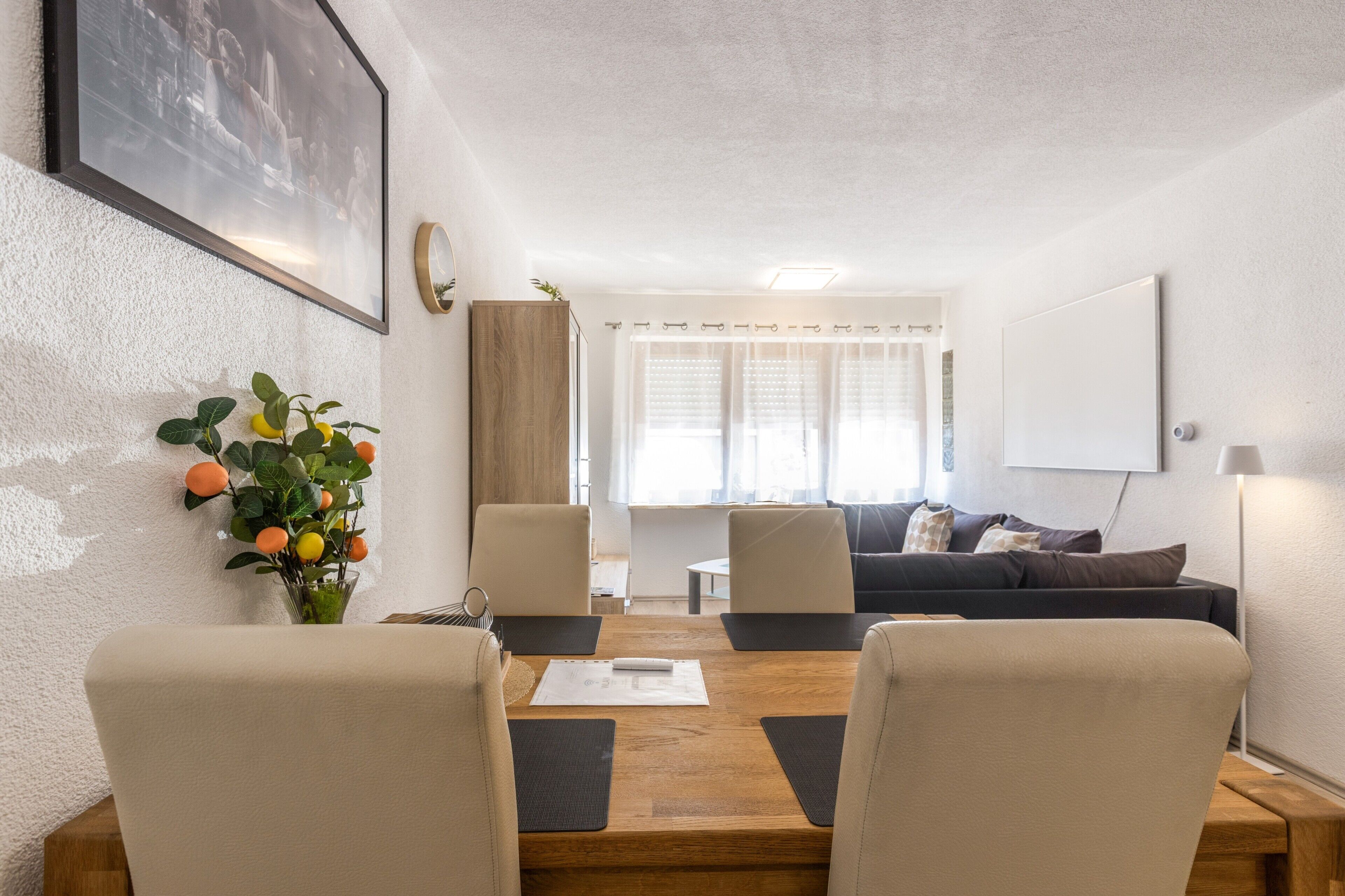 Ein modernes Wohnzimmer mit einem Holzesstisch, zwei Stühlen, einer Couch und einem großen Fenster mit Vorhängen.