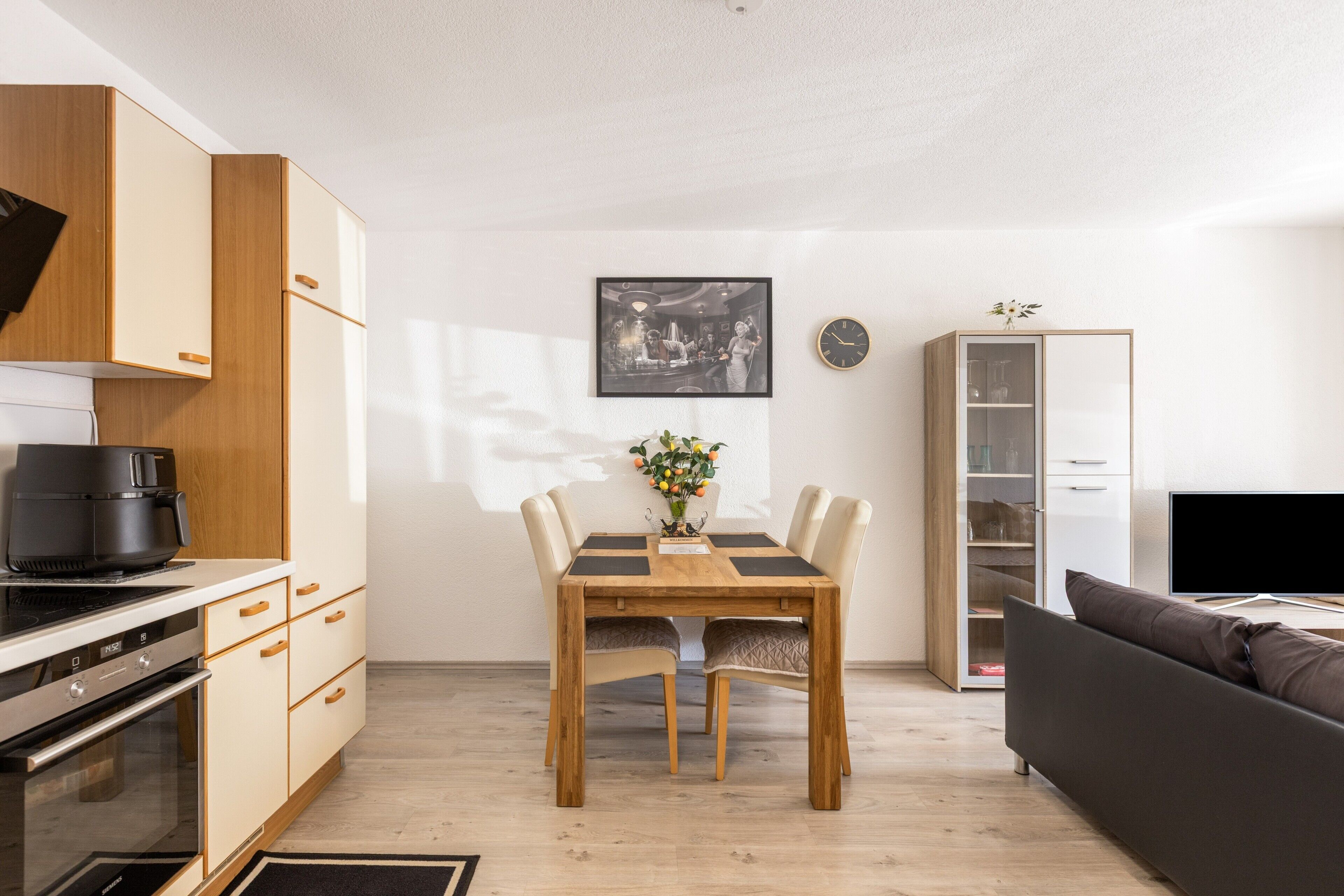 Eine moderne Küche mit Einbauofen und Kaffeemaschine, ein Essbereich mit Holztisch und Stühlen, eine Couch und ein Fernseher.