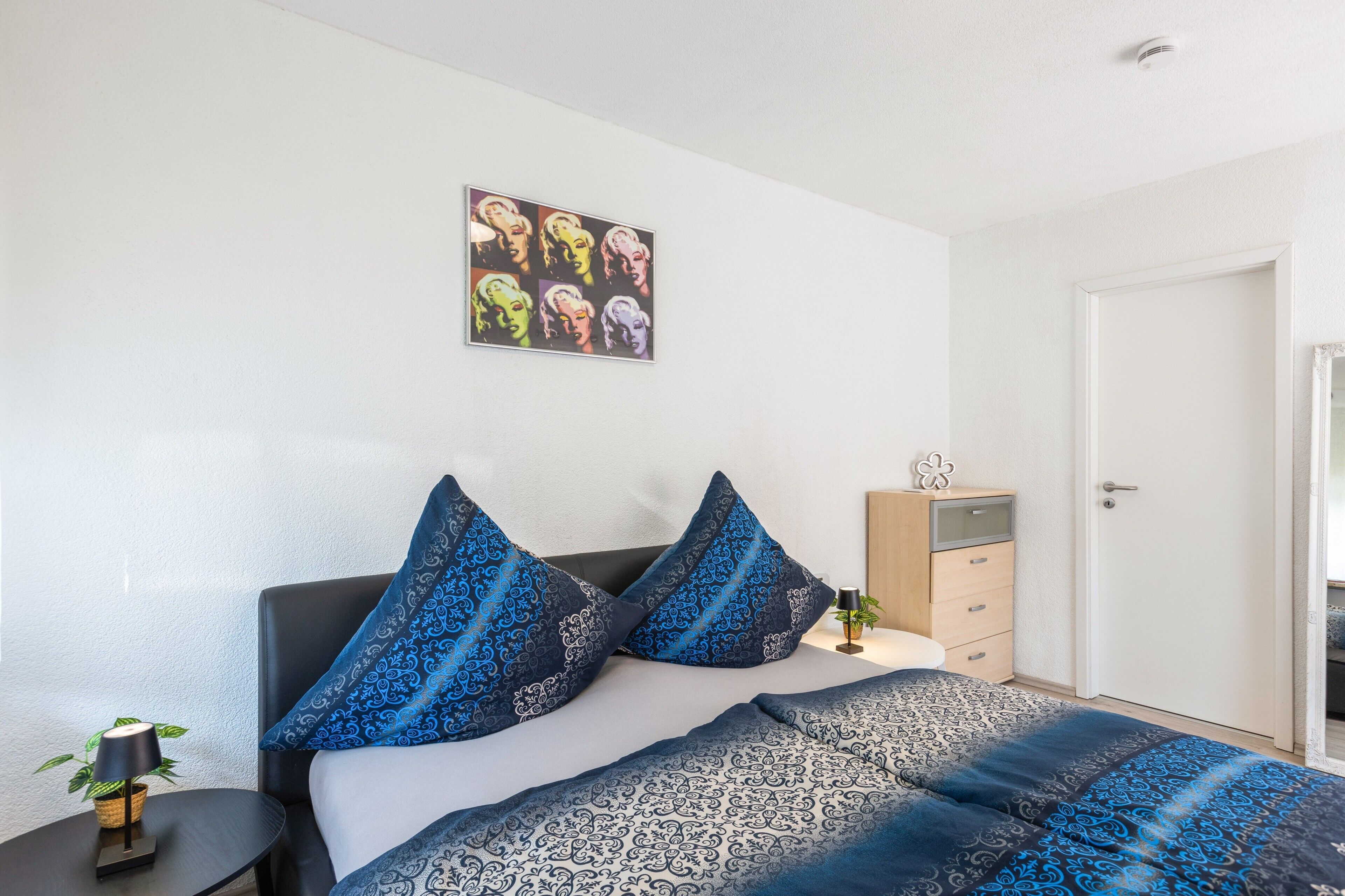 Une chambre à coucher avec un lit, une table de chevet avec une lampe, une commode et une porte.