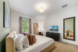A hotel room with a bed, a TV, a desk, and a window with curtains. - New Listing! Casa Solara - Private Pool, Spa, Super Close to Disney World! (Kissimmee)