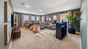 A modern living room with a sectional sofa, a coffee table, a bean bag, a desk with a computer, and a large potted plant. - New Listing! Casa Solara - Private Pool, Spa, Super Close to Disney World! (Kissimmee)