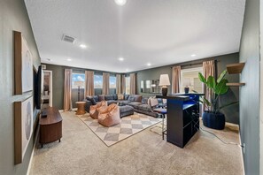 A modern living room with a sectional sofa, a coffee table, a bean bag, a desk with a computer, and a large potted plant. - New Listing! Casa Solara - Private Pool, Spa, Super Close to Disney World! (Kissimmee)