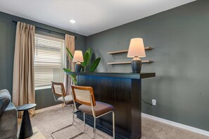 A room with a dark wood reception desk, two chairs, a small table, a potted plant, and a window with blinds. - New Listing! Casa Solara - Private Pool, Spa, Super Close to Disney World! (Kissimmee)