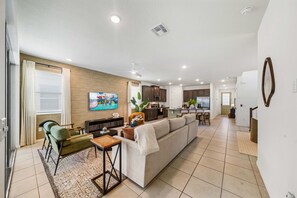A modern living room with a sofa, a coffee table, and a TV. There is a kitchen area with cabinets and a refrigerator. - New Listing! Casa Solara - Private Pool, Spa, Super Close to Disney World! (Kissimmee)