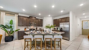 A modern kitchen with a central island, stainless steel appliances, and a potted plant. - New Listing! Casa Solara - Private Pool, Spa, Super Close to Disney World! (Kissimmee)
