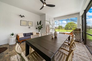 A dining area with a table, chairs, a ceiling fan, and a view of a green landscape through a glass door. - New Listing! Casa Solara - Private Pool, Spa, Super Close to Disney World! (Kissimmee)