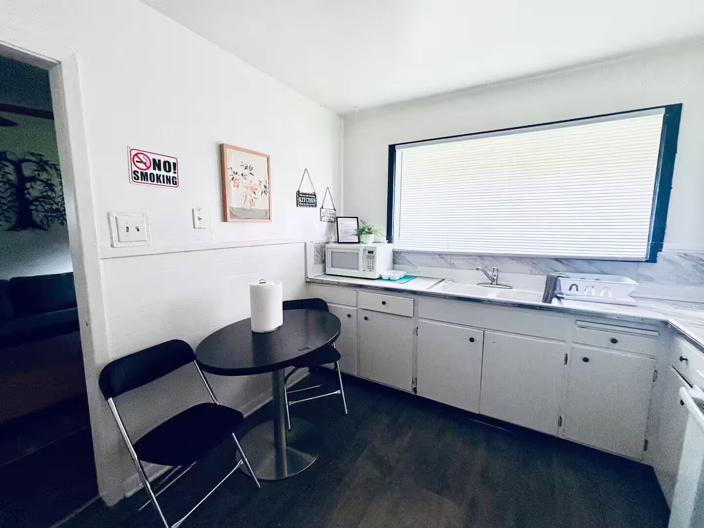 A compact kitchen with a dining area, a microwave, a sink, and a window with blinds.