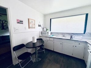 Une cuisine compacte comprenant un coin repas, un four à micro-ondes, un évier et une fenêtre avec des stores.