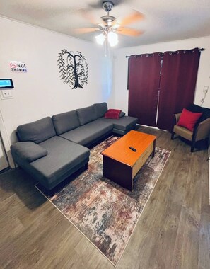 Un salon avec un canapé d’angle gris, une table basse en bois et un rideau rouge.