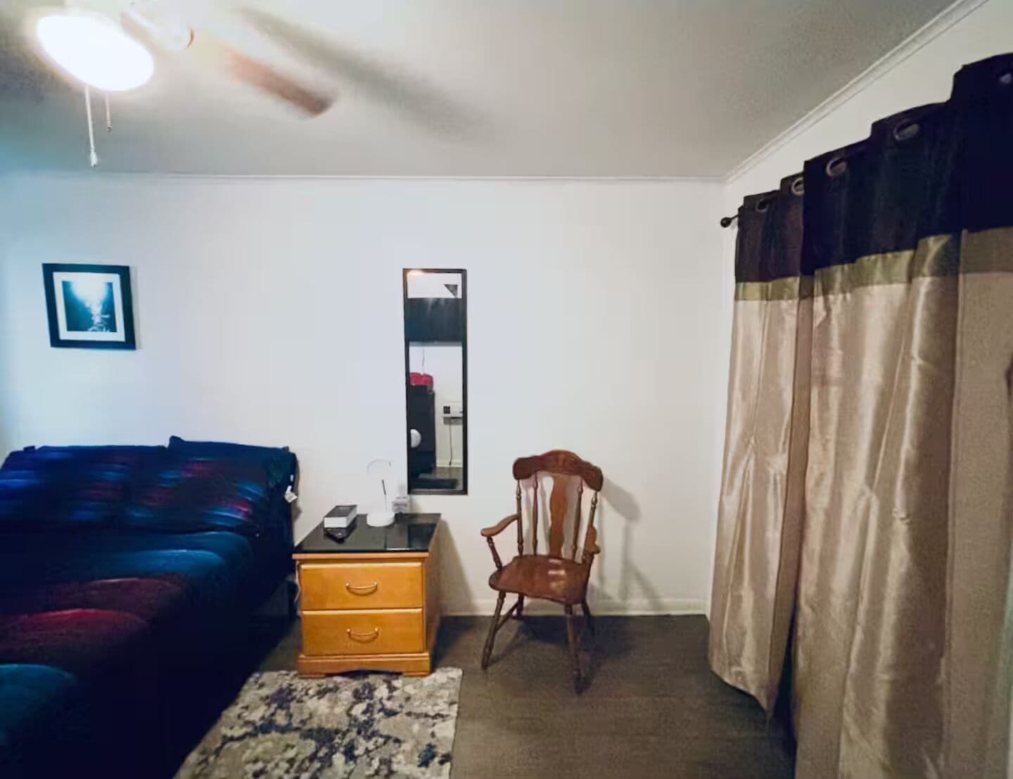 A room with a bed, a chair, a dresser, a mirror, and a window with curtains.