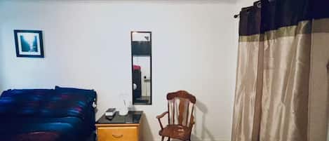 A room with a bed, a chair, a dresser, a mirror, and a window with curtains.
