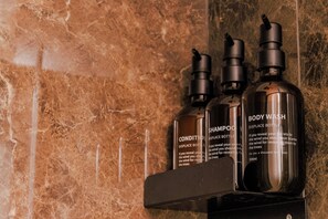 Three bottles of body wash on a black shelf against a marble wall. - Comfortable apartment in the historic center of Santo Stefano (Bologna)