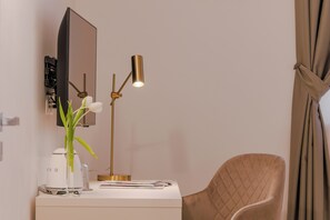 A modern hotel room with a desk, a lamp, a mirror, a chair, and a window with curtains. - Comfortable apartment in the historic center of Santo Stefano (Bologna)
