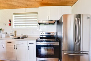 A kitchen with white cabinets, a stainless steel refrigerator, a stove, and a coffee maker.