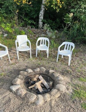 A fire pit with logs, surrounded by four white plastic chairs.