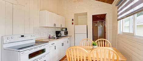 Una cocina compacta con muebles blancos, estufa, microondas y ventilador de techo.