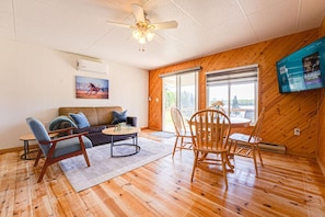 A room with a wooden floor, a ceiling fan, a sofa, a coffee table, and a TV mounted on the wall.