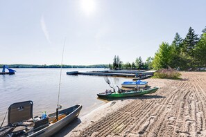 Un paisaje junto al lago con barcos amarrados cerca de la orilla, una playa de arena y árboles al fondo.
