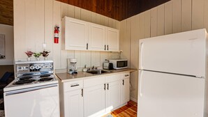 Una cocina con gabinetes blancos, estufa, microondas y refrigerador.