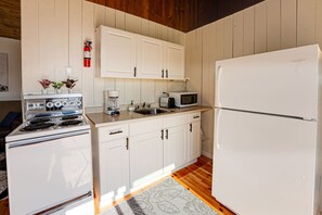 A kitchen with white cabinets, a stove, a microwave, and a refrigerator.