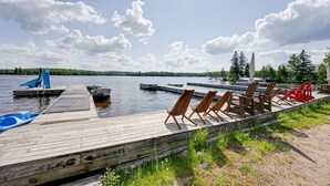 Un muelle de madera con barcos, sillas de descanso y una pequeña piscina.