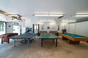 A room with a ping pong table, a foosball table, and a pool table.