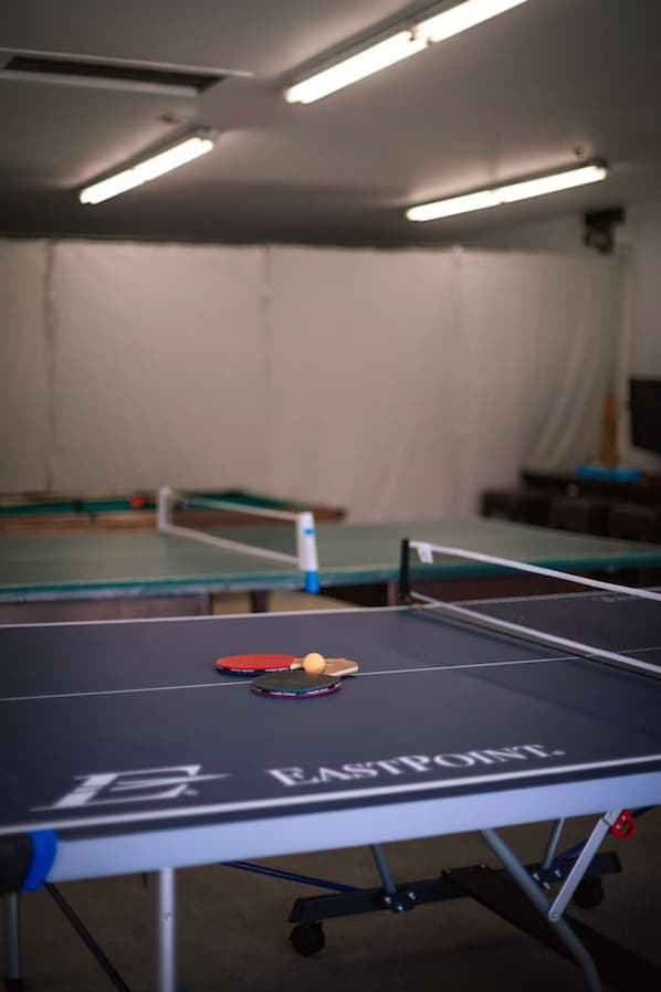 Une table de ping-pong avec une balle et une raquette, une deuxième table en arrière-plan et une structure ressemblant à une tente.