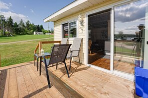 A deck with outdoor furniture, a sliding glass door to a kitchen, and a grassy yard.